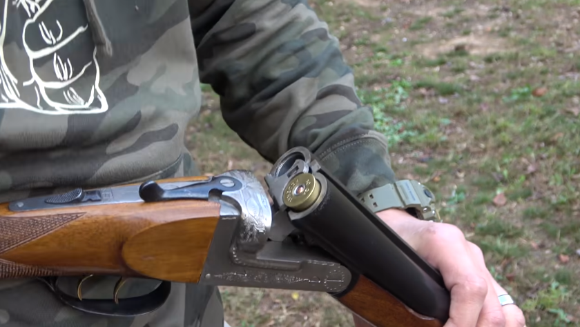 hand holding opened double barrel shotgun with one cartridge